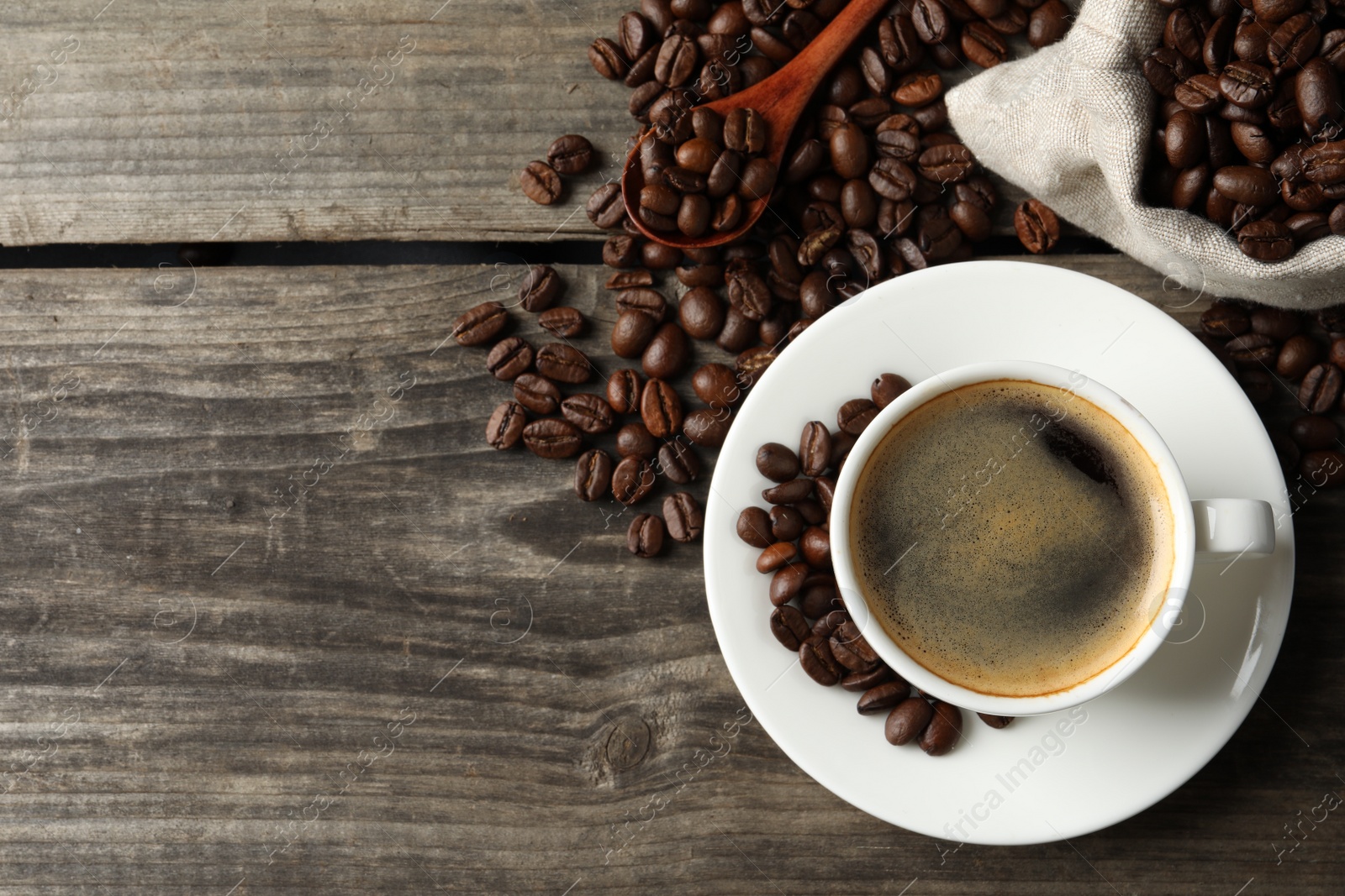 Photo of Cup of hot aromatic coffee and roasted beans on wooden table, flat lay. Space for text