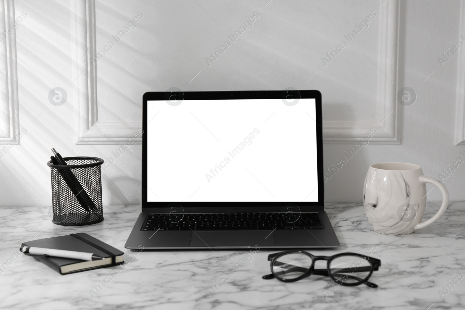 Photo of Office workplace with computer, glasses, cup and stationery on marble table near white wall