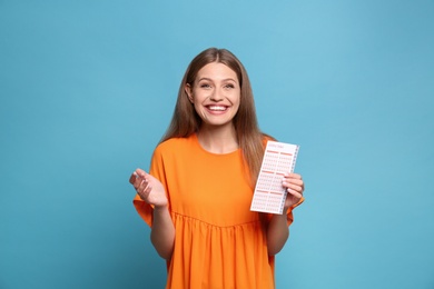 Portrait of happy young woman with lottery ticket on light blue background