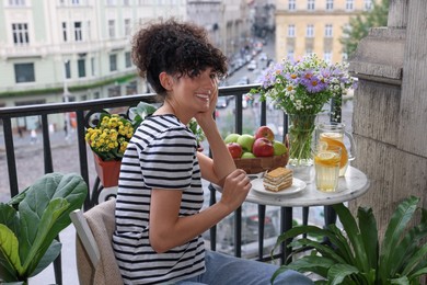 Young woman eating piece of cake at table on balcony with beautiful houseplants