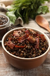 Photo of Delicious lentils with bacon in bowl on wooden table, closeup