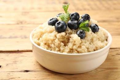 Photo of Tasty quinoa porridge with blueberries and mint in bowl on wooden table, closeup