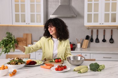 Photo of Woman cooking healthy vegetarian meal at white marble table in kitchen