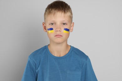 Photo of Little boy with drawing of Ukrainian flag on face against light grey background