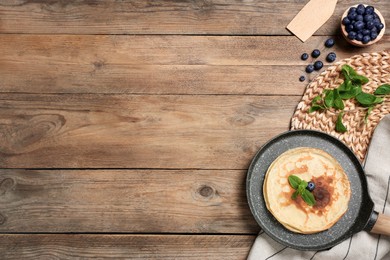 Photo of Delicious crepes with mint and blueberries on wooden table, flat lay. Space for text