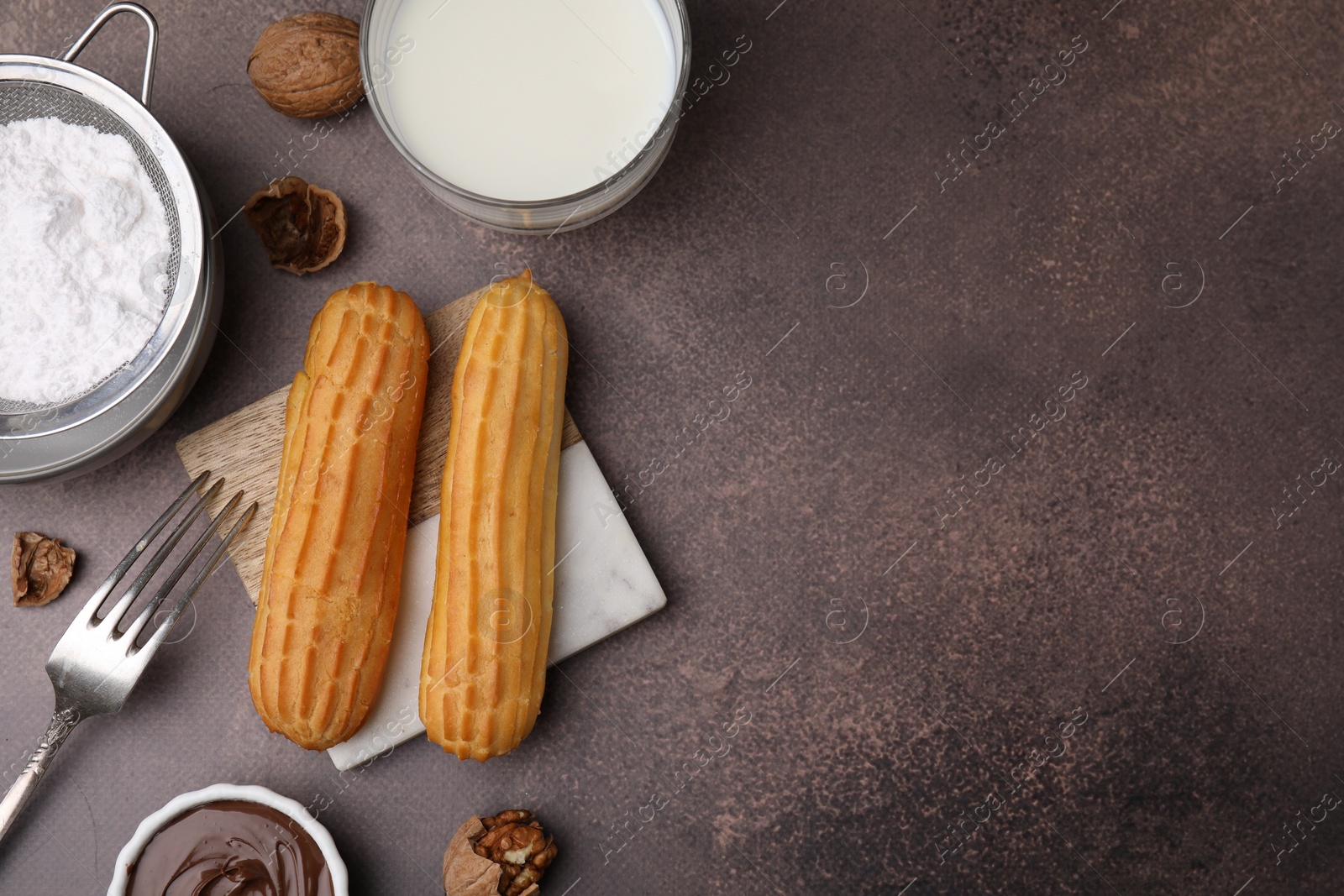 Photo of Delicious eclairs, chocolate paste, milk and walnuts on grey table, flat lay. Space for text