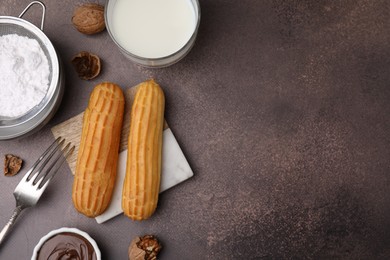 Delicious eclairs, chocolate paste, milk and walnuts on grey table, flat lay. Space for text