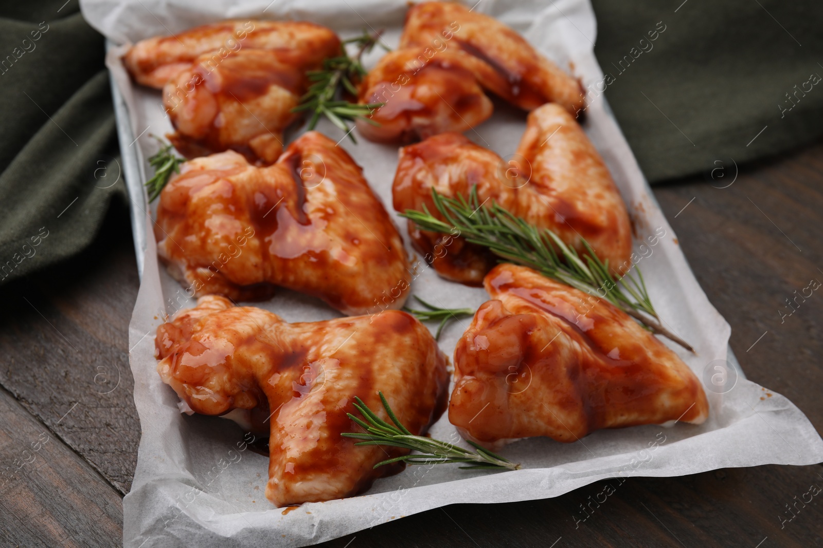 Photo of Raw marinated chicken wings and rosemary on wooden table, closeup