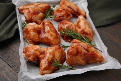 Photo of Raw marinated chicken wings and rosemary on wooden table, closeup