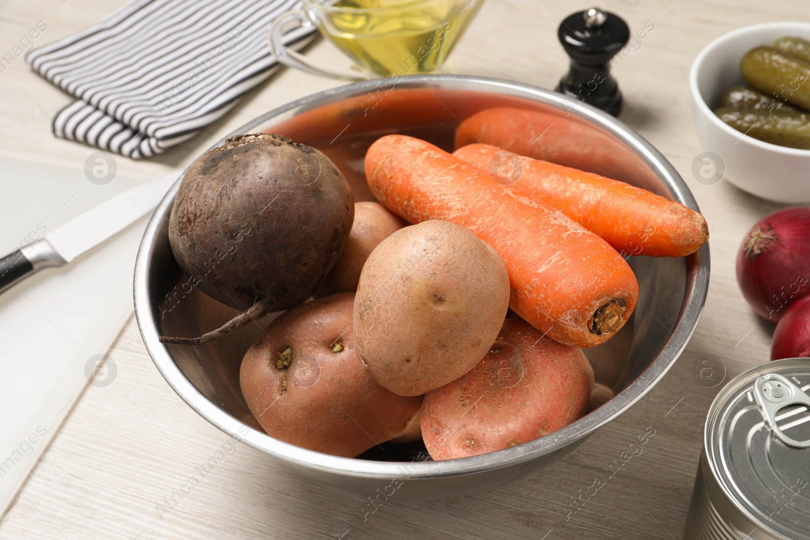 Photo of Bowl with many fresh vegetables and other ingredients on white wooden table, closeup. Cooking vinaigrette salad