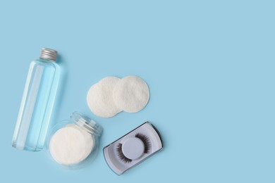 Photo of Bottle of makeup remover, cotton pads and false eyelashes on light blue background, flat lay. Space for text