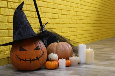 Photo of Pumpkin with drawn creepy face and burning candles near yellow brick wall in hallway. Halloween decor