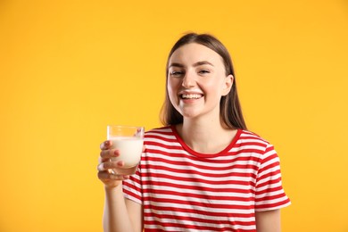 Happy woman with milk mustache holding glass of tasty dairy drink on orange background