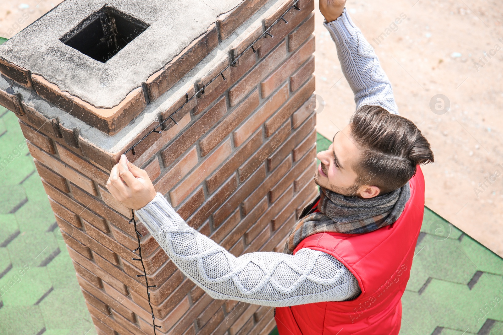 Photo of Young man decorating chimney with Christmas lights