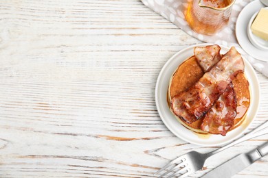 Delicious pancakes with maple syrup and fried bacon on white wooden table, flat lay. Space for text
