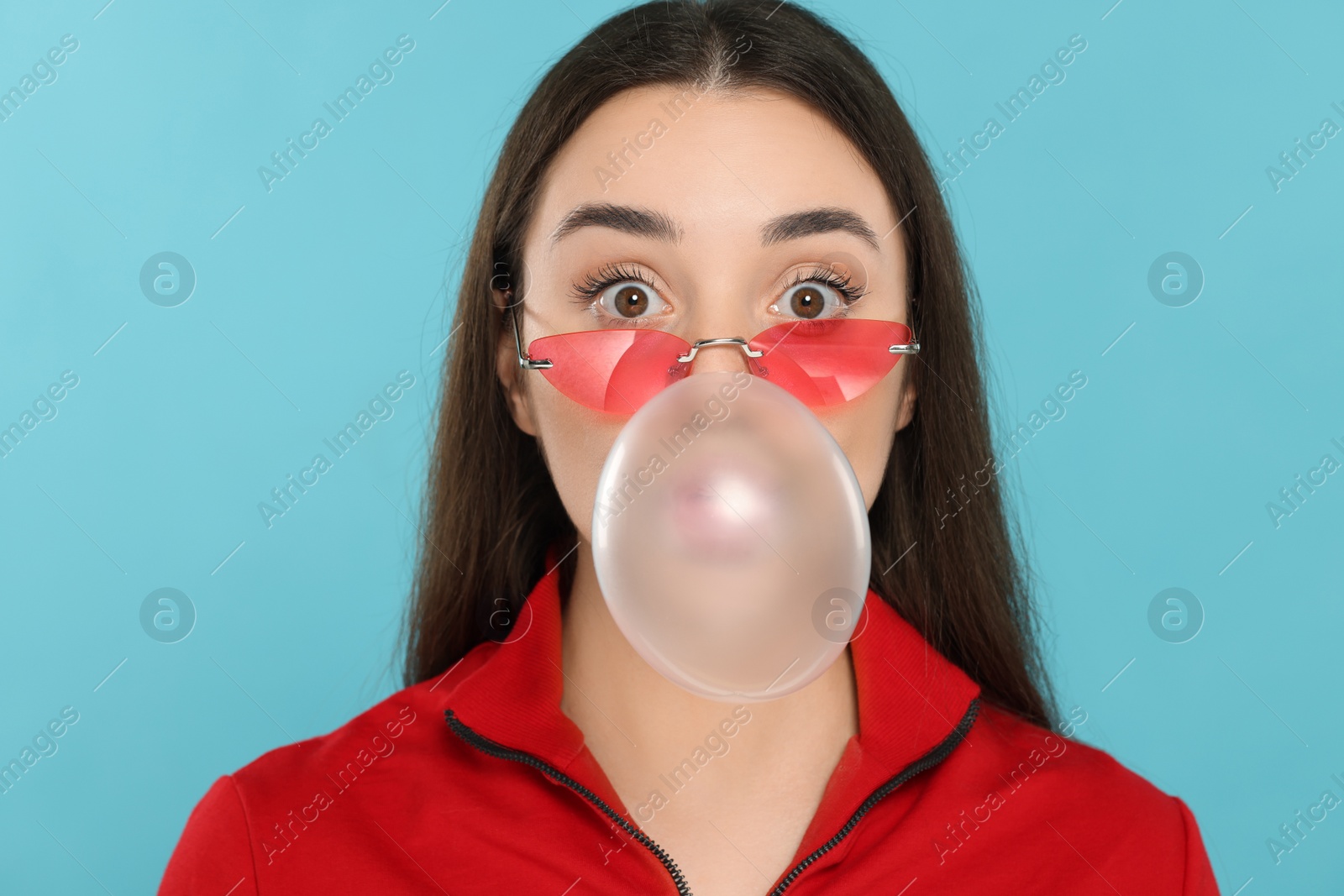 Photo of Beautiful young woman blowing bubble gum on light blue background