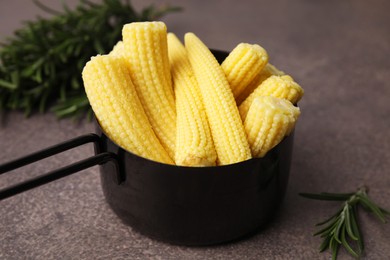 Tasty fresh yellow baby corns in dish on brown table, closeup