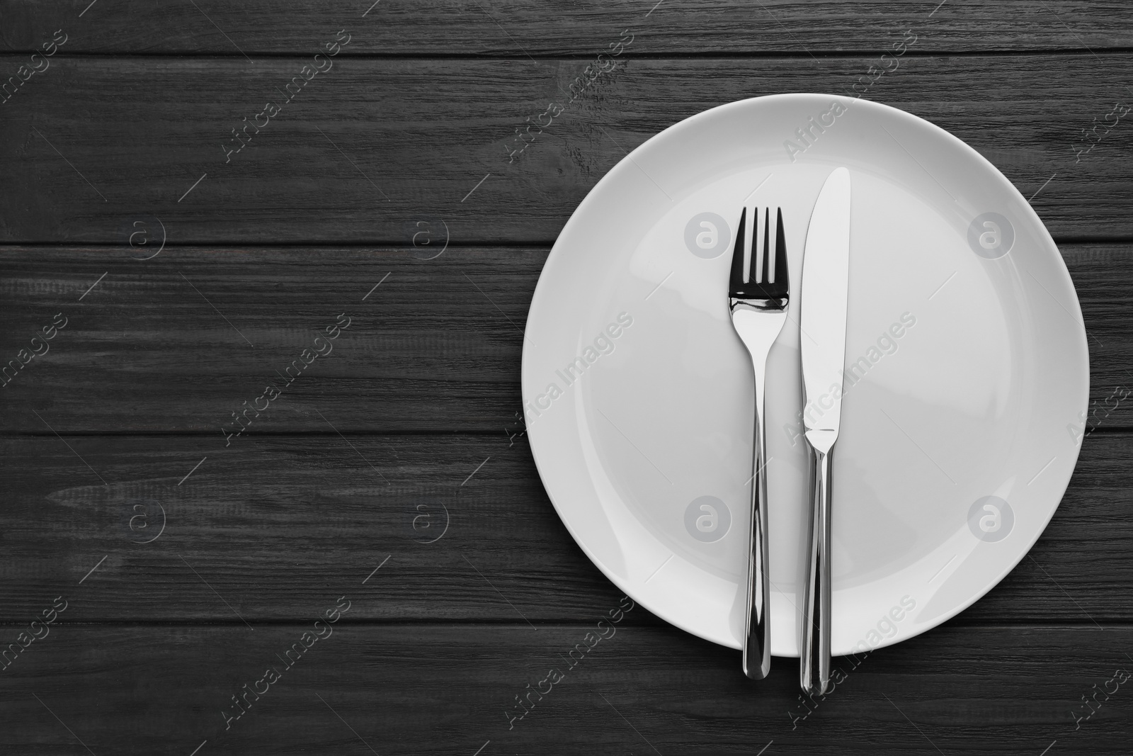 Photo of Clean plate and cutlery on black wooden table, top view