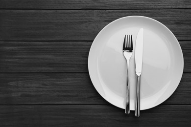 Photo of Clean plate and cutlery on black wooden table, top view