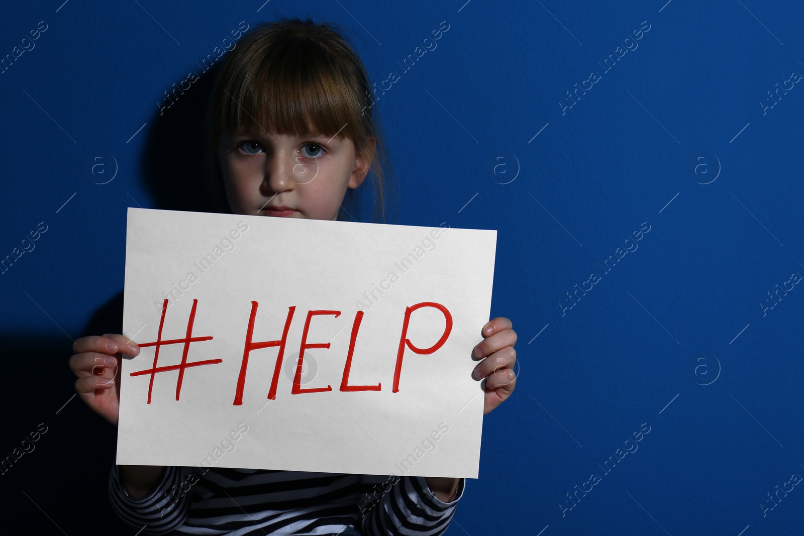 Photo of Abused little girl with hashtag HELP near blue wall. Domestic violence concept