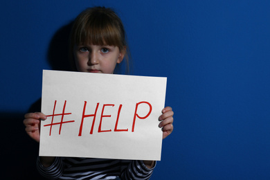 Abused little girl with hashtag HELP near blue wall. Domestic violence concept
