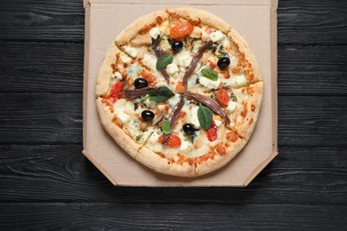 Photo of Tasty pizza with anchovies, basil and olives on black wooden table, top view