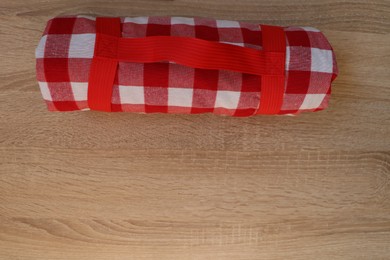 Folded checkered picnic blanket on wooden table, top view. Space for text