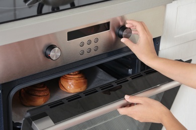 Young woman baking buns in electric oven, closeup