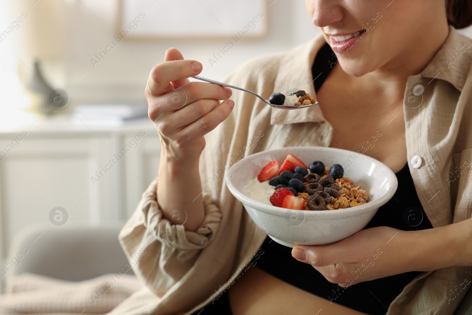 Photo of Woman eating tasty granola with fresh berries and yogurt at home, closeup