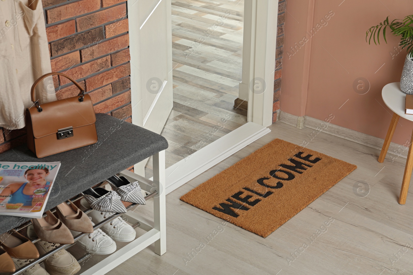 Photo of Doormat with word Welcome near shoe rack on white wooden floor in hall