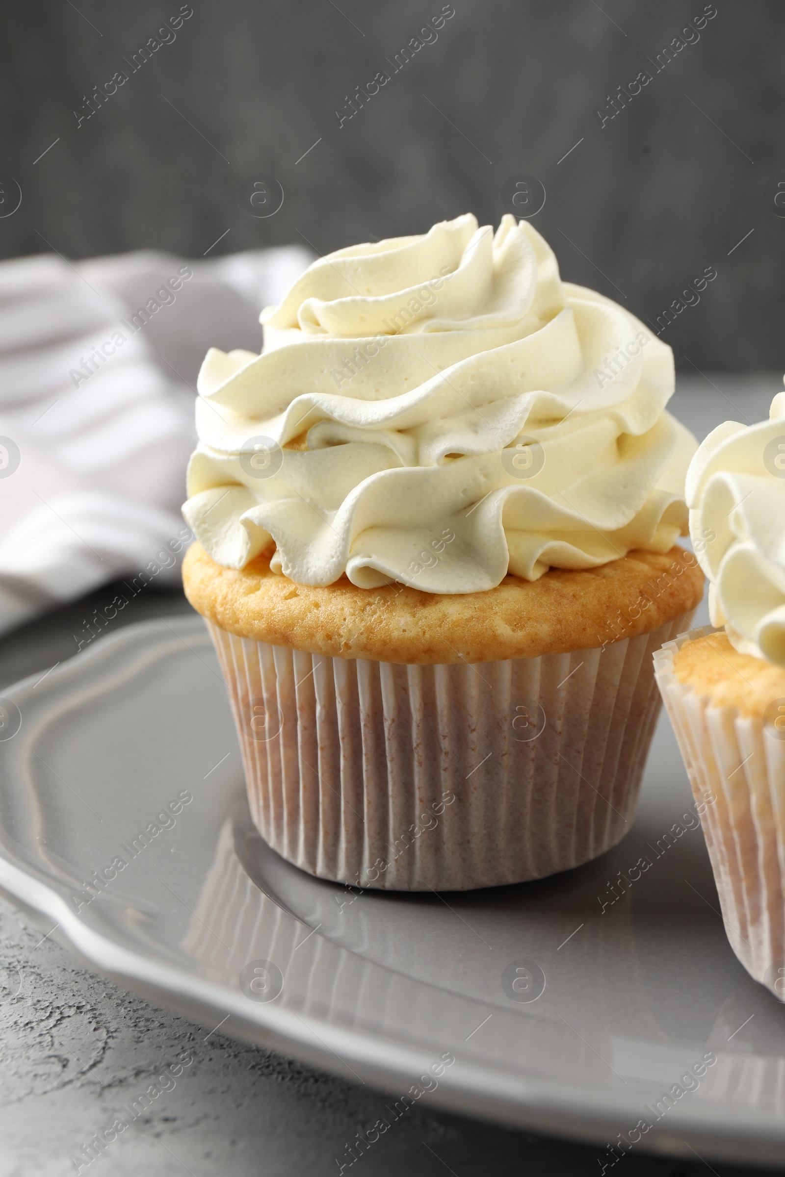 Photo of Tasty cupcakes with vanilla cream on grey table, closeup