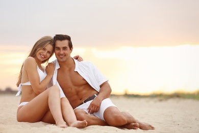 Happy young couple relaxing together on sea beach at sunset