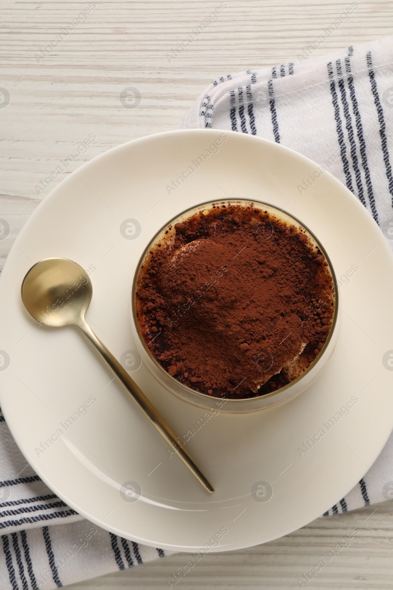 Photo of Delicious tiramisu in glass and spoon on white wooden table, top view