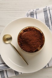 Delicious tiramisu in glass and spoon on white wooden table, top view