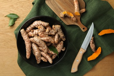 Many raw turmeric roots and knife on wooden table, flat lay