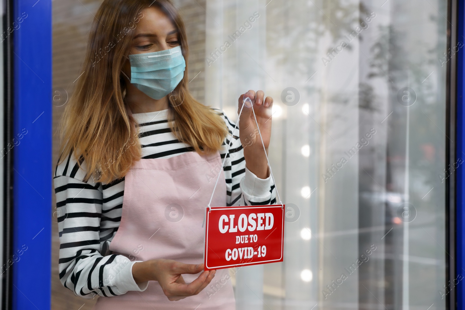 Photo of Business owner in mask hanging red sign with text Closed Due To Covid-19 onto glass door. Coronavirus quarantine