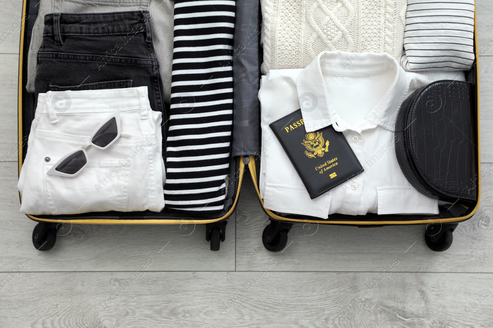Photo of Open suitcase with clothes, passport and accessories on floor, top view