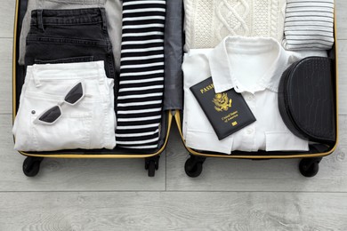 Open suitcase with clothes, passport and accessories on floor, top view