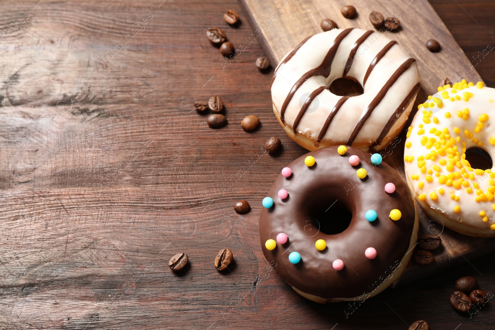 Photo of Yummy donuts with colorful sprinkles on wooden table, space for text