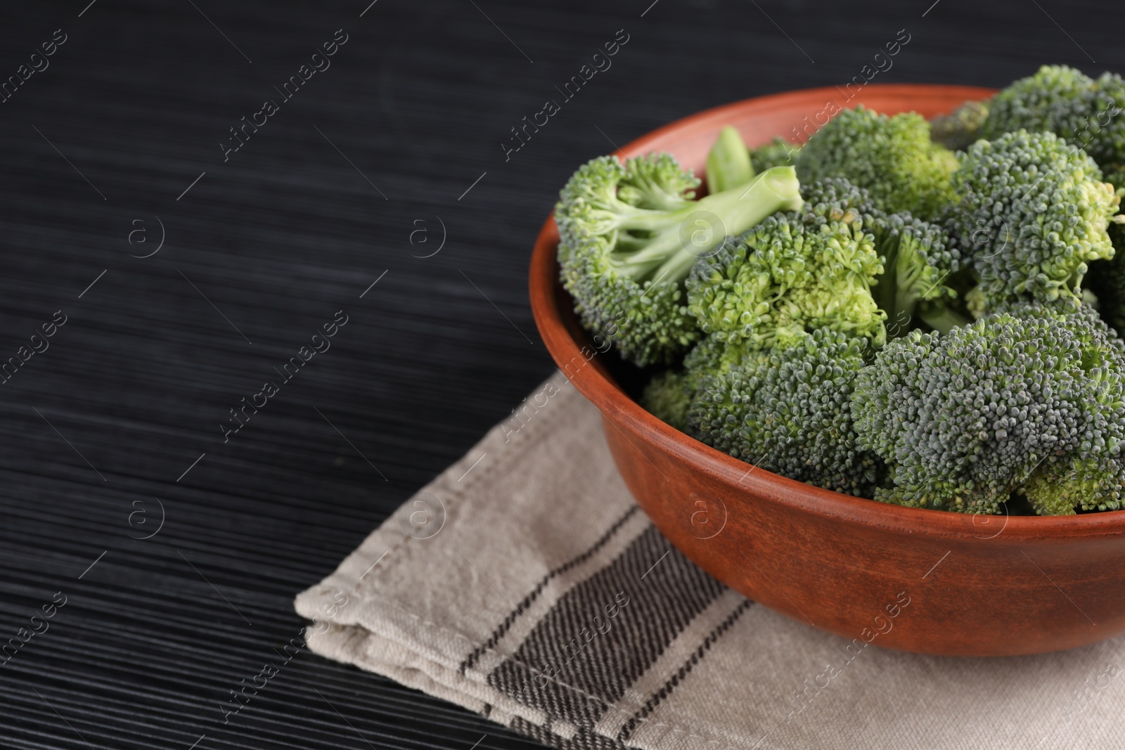 Photo of Bowl with fresh raw broccoli on black wooden table, closeup. Space for text