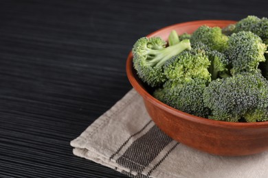 Bowl with fresh raw broccoli on black wooden table, closeup. Space for text