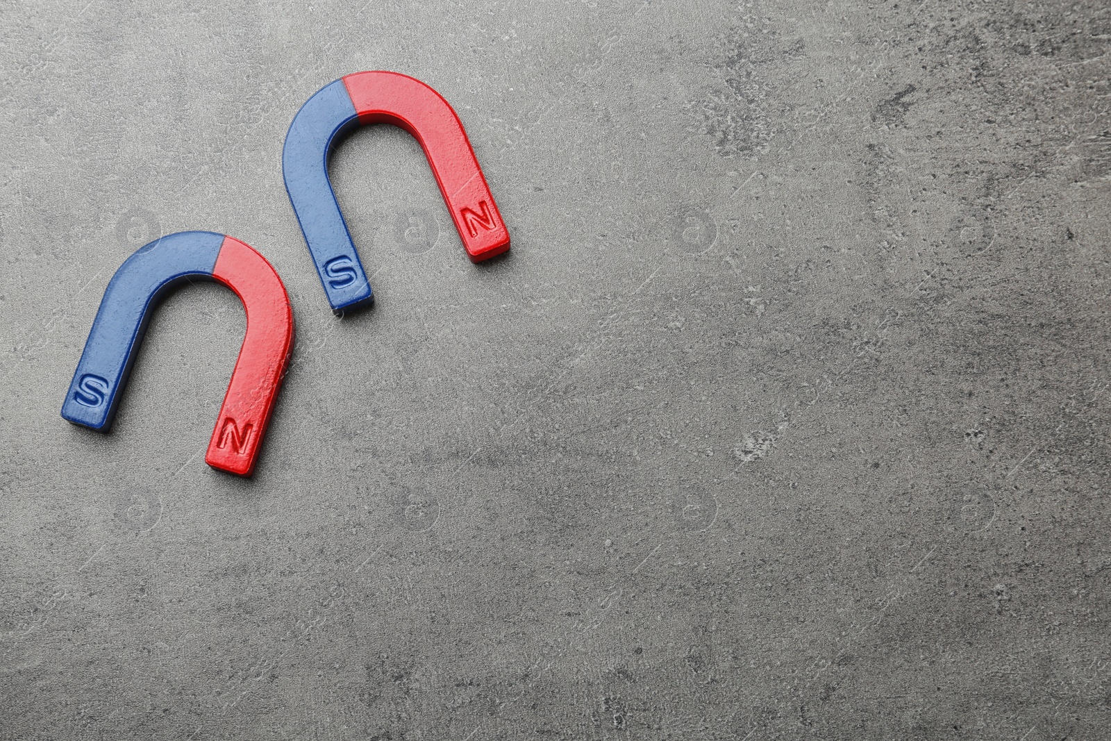 Photo of Red and blue horseshoe magnets on grey background, top view with space for text