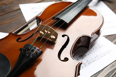 Photo of Beautiful violin, bow and note sheets on wooden table, closeup