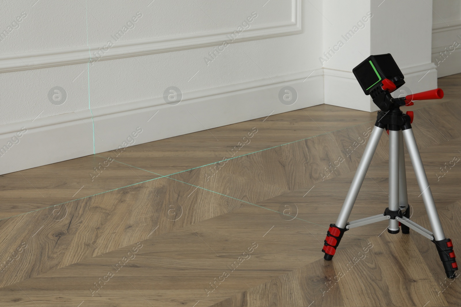 Photo of Cross line laser level with tripod on wooden floor indoors