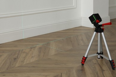 Photo of Cross line laser level with tripod on wooden floor indoors
