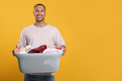 Photo of Happy man with basket full of laundry on orange background. Space for text