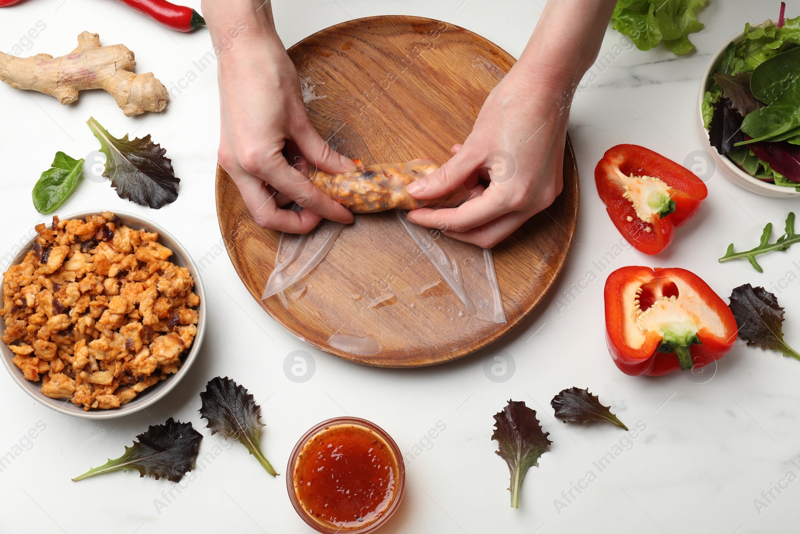 Photo of Woman making tasty spring roll at white marble table, top view