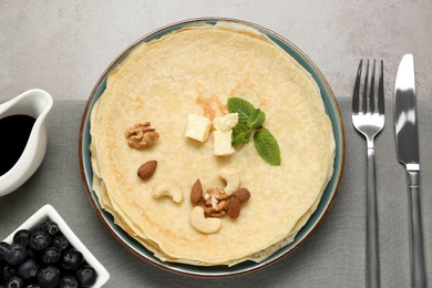 Photo of Delicious crepes with butter, mint and nuts served on light grey table, flat lay