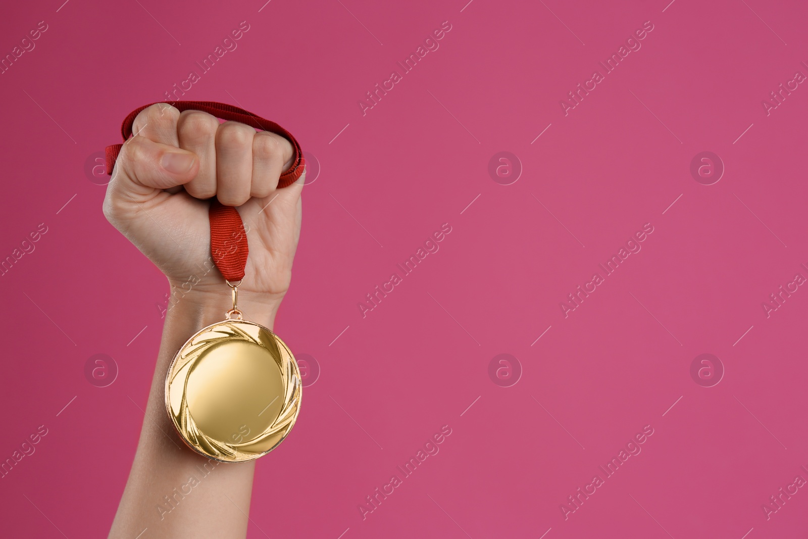 Photo of Woman holding golden medal on pink background, closeup. Space for design