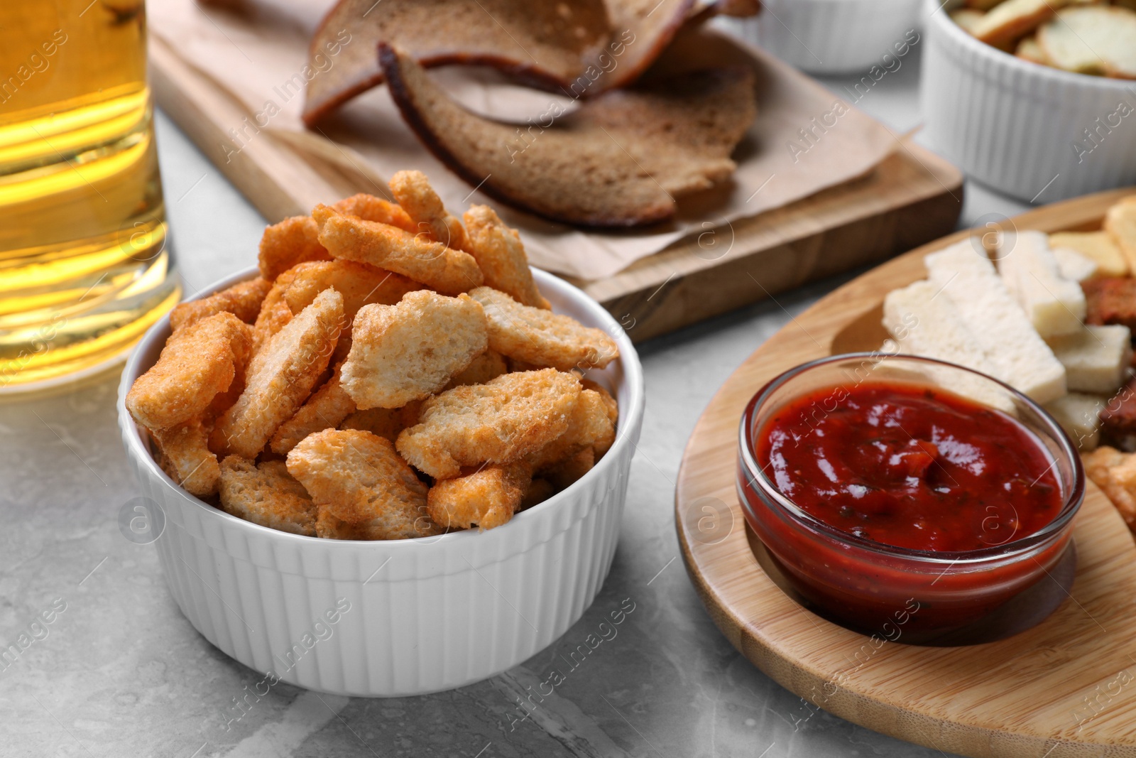 Photo of Different crispy rusks with dip sauce on light table, closeup